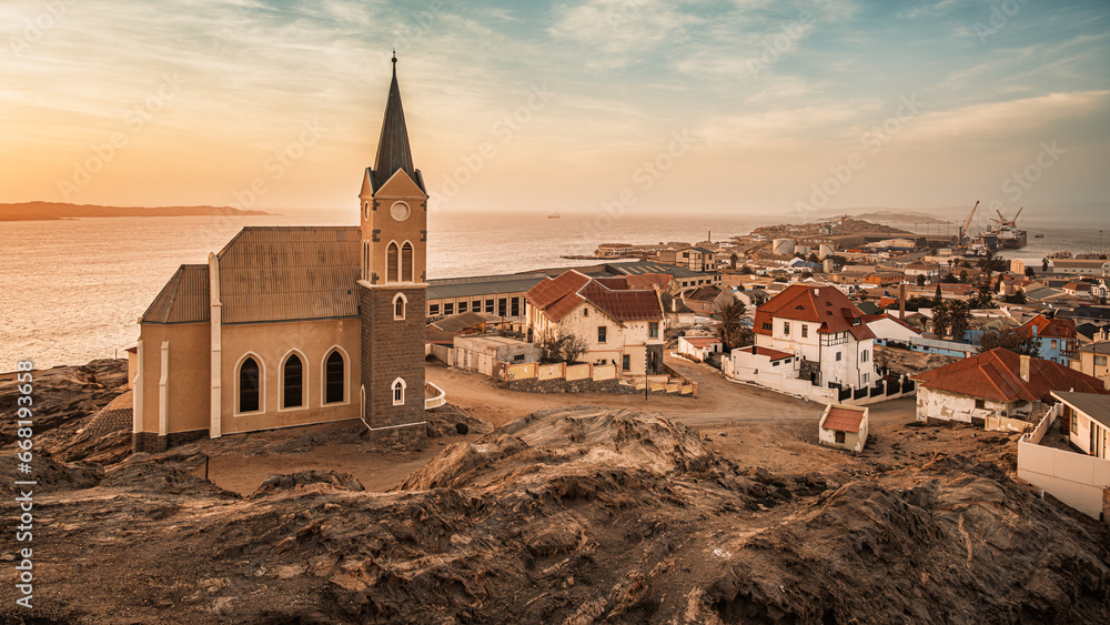 Panoramic view of Luderitz, Namibia, showcasing the Felsenkirche, the historic city Lutheran Church, and the German-style houses and buildings extending towards the port and the Atlantic Ocean. - obrazy, fototapety, plakaty 