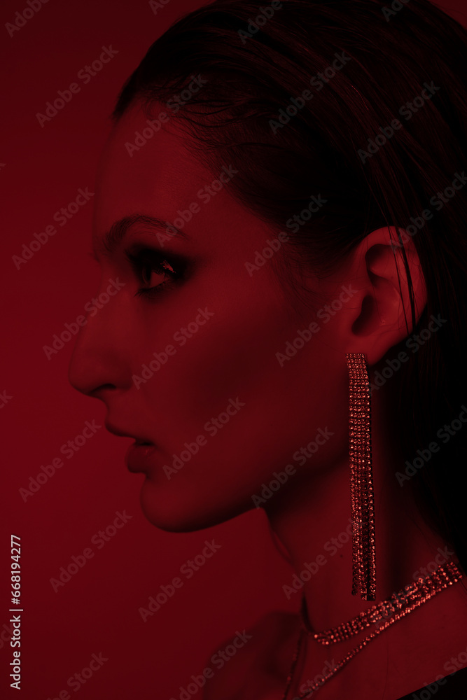 Stylish female model in bright colorful lights posing in studio. Portrait of a beautiful girl with fashionable shining makeup. Beautiful jewelry and accessories. Neon red color. Stylish female model in bright colorful lights posing in studio. Portrait of a beautiful girl with fashionable shining makeup. Beautiful jewelry and accessories. Neon red color.