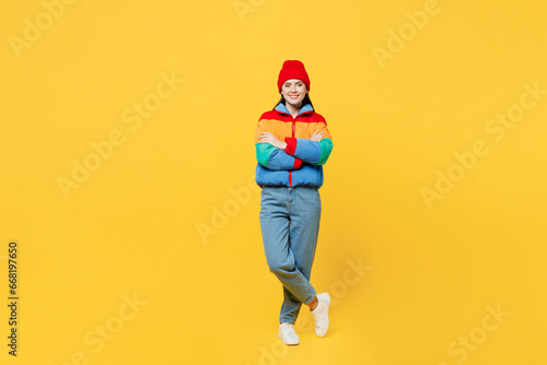 Full body young smiling cheerful woman she wears padded windbreaker jacket red hat casual clothes hold hands crossed folded look camera isolated on plain yellow background studio. Lifestyle concept. photo