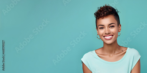 Smimilg young woman with dark skin and short groomed hair isolated on flat turquoise pastel background with copy space. Model for banner of cosmetic products, beauty salon and dentistry