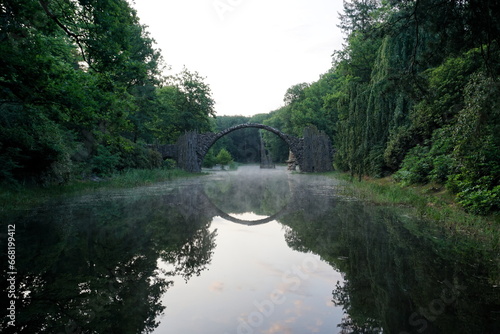 Devil's bridge in Kromlau, Germany during blue hour with its reflection in the water and white haze over the water photo