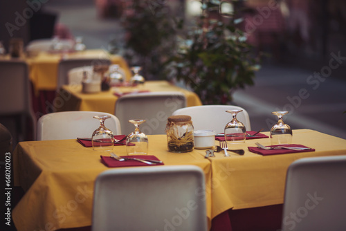 Street view of a coffee terrace with tables and chairs in europe. Outdoor restaurant in Italy. Empty glasses set in cafe with beautiful italian street at the background. Food, travel and vacation.