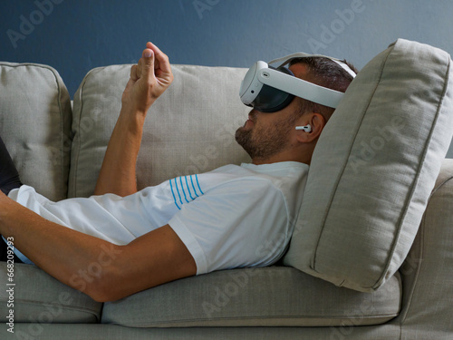 Man using virtual mixed reality glasses, wearing new generation vr headset for entertainment lying down on sofa.