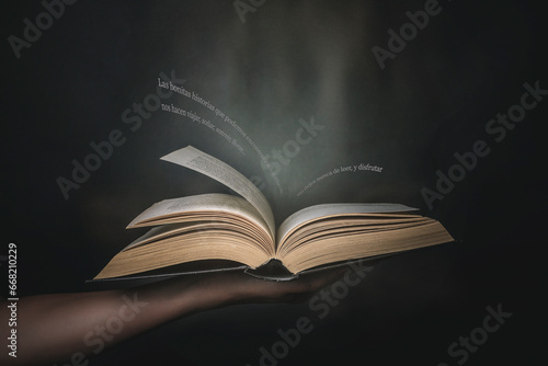 Person's hand holding an open book with  Spanish motivational text flying off the page photo