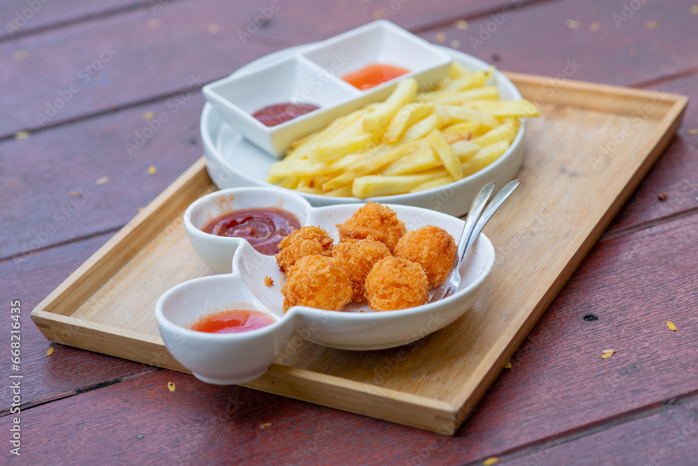 Naklejka premium French fries and cheese balls on a white plate on a tray and a wooden board background Contains ketchup and chili sauce