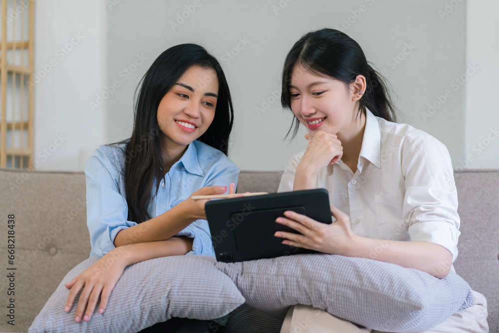 Two millennial Asian females looking at a digital tablet together in a living room. Two millennial Asian females looking at a digital tablet together in a living room.