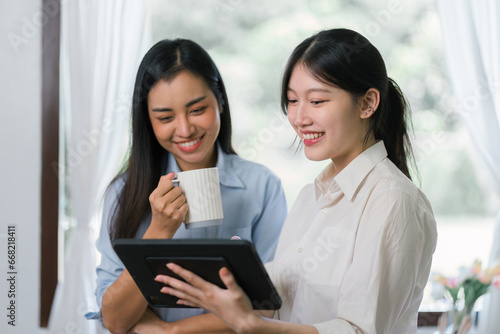 Two millennial Asian females looking at a digital tablet together in a living room.