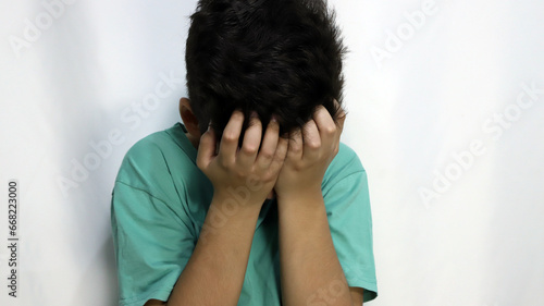 Sad child covering his face as a sign of depression, crying, anger. Child with shame. Boy angry and crying hiding his face. Concept of sensitivity, protection, shyness, anger. photo