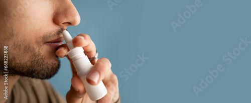 Foto Man using nasal spray for a runny nose and congestion isolated on a blue background, close-up