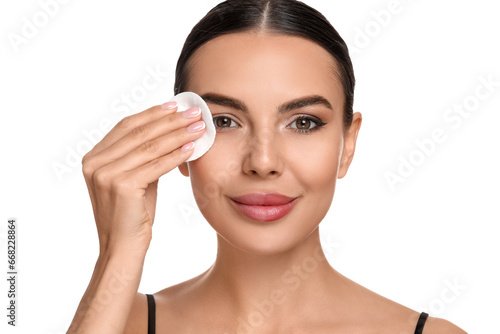 Beautiful woman removing makeup with cotton pad on white background