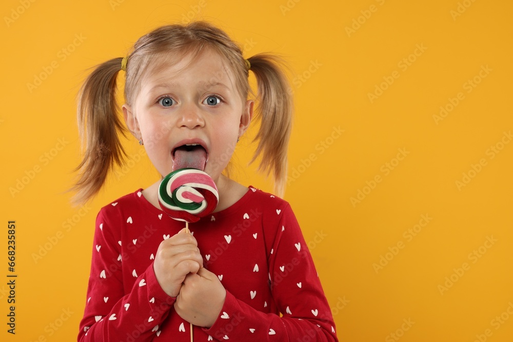 Portrait of cute girl licking lollipop on orange background, space for text Portrait of cute girl licking lollipop on orange background, space for text