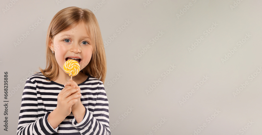 Portrait of cute girl licking lollipop on light grey background, space for text Portrait of cute girl licking lollipop on light grey background, space for text