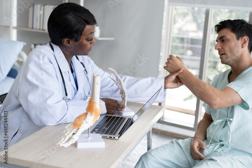 African American Doctor or Physiotherapist working examining treating of caucasian patient  checking arm  in clinic 