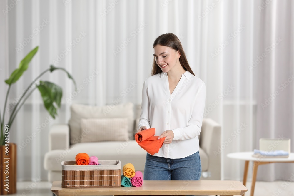 Smiling woman rolling shirt at table in room. Organizing clothes Smiling woman rolling shirt at table in room. Organizing clothes