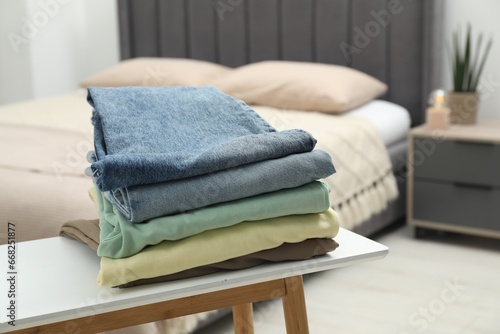 Stack of different folded clothes on bedside bench indoors, closeup