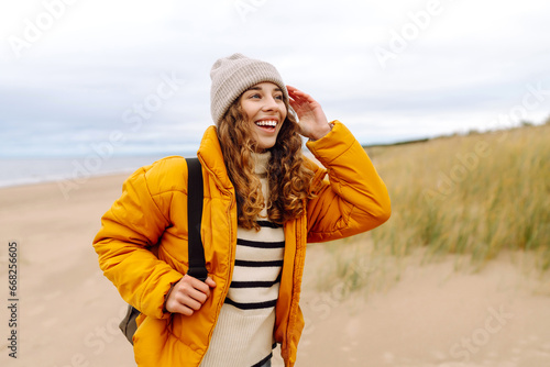 A beautiful young tourist woman in a yellow jacket with a backpack enjoys life near the sea. Travel, lifestyle, adventure.