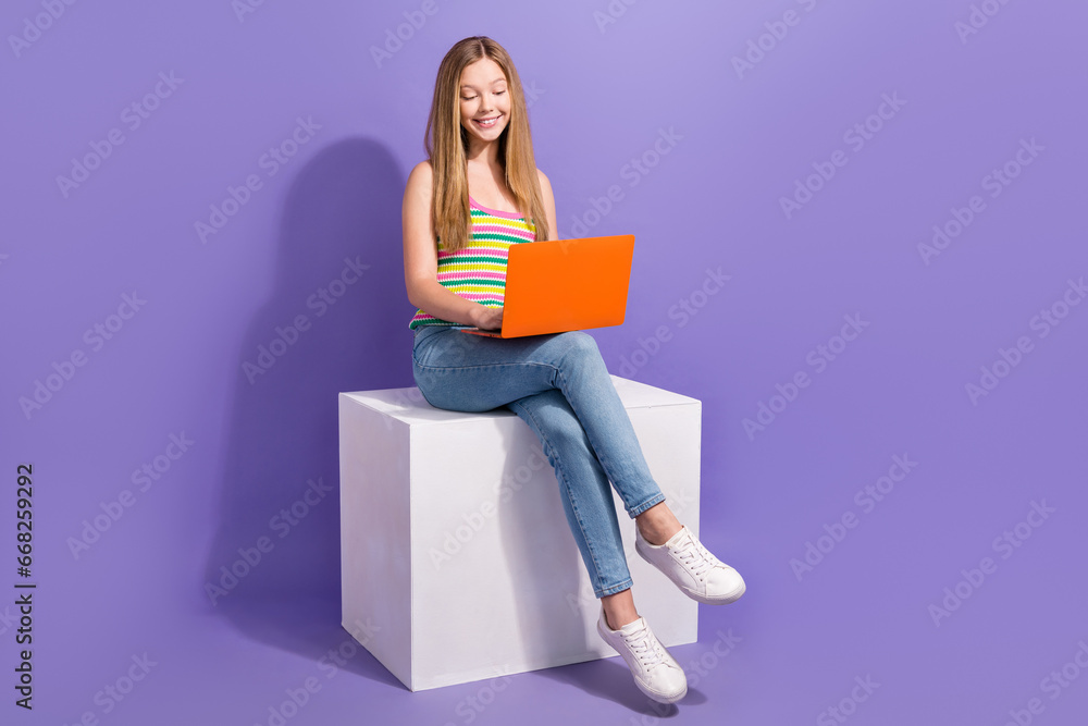 Full body photo of cute teen blonde woman laptop sit platform dressed stylish striped clothes isolated on violet color background