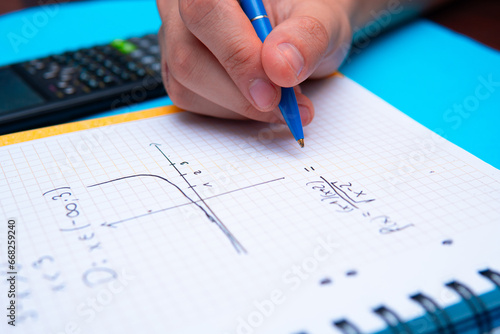 A close-up of a student solving math problems. Notebook with math tasks on a blue background. Solving math problems to practice