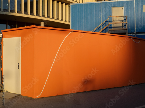 Orange wooden wall in font of a blue barack.