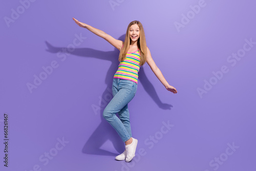 Full size photo of pretty teenager blonde girl flying hands wings dressed stylish striped outfit isolated on violet color background