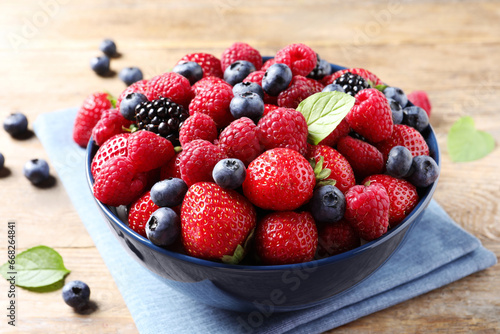 Different fresh ripe berries in bowl on wooden table  closeup