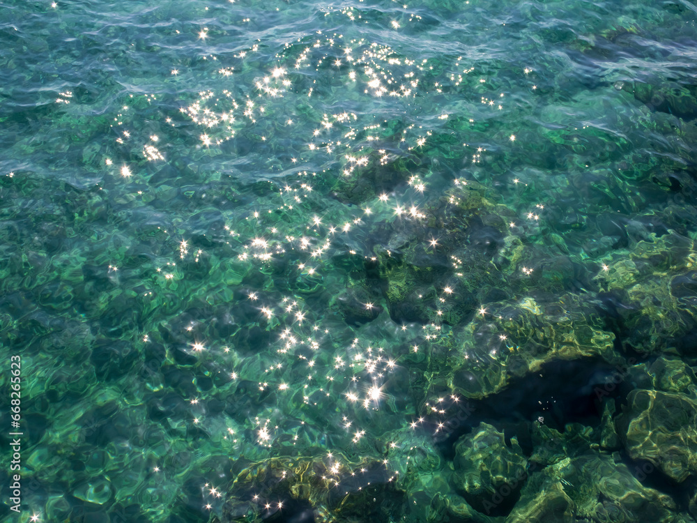 Gleaming green sea water with shiny sparkles and rocks underwater