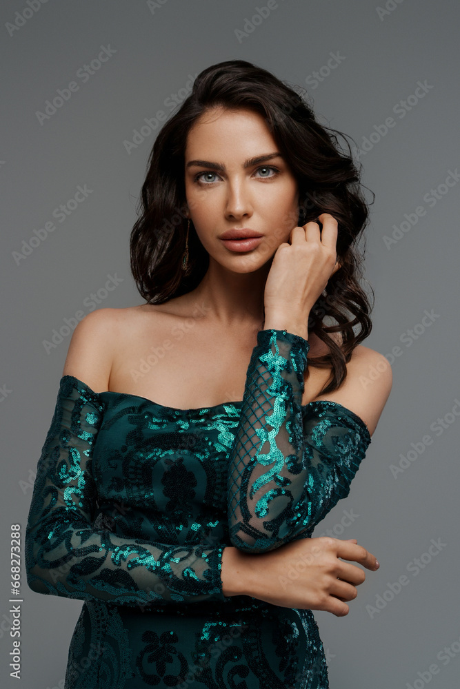 Stunning brunette with a voluminous hairstyle in a graceful green evening gown against a gray backdrop Stunning brunette with a voluminous hairstyle in a graceful green evening gown against a gray backdrop