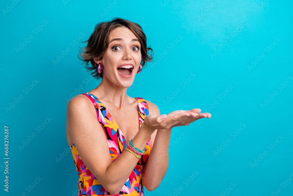 Portrait of impressed ecstatic adorable person wear colorful dress hold object on arms empty space isolated on blue color background