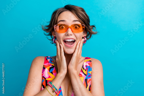Portrait of ecstatic overjoyed person with bob hairdo wear colorful dress in sunglass astonihsed staring isolated on blue color background