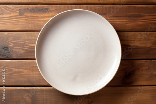 Top view of an empty artistic ceramic Glazed earthenware white fancy shape plate, golden cutlery on side, leave on a scandinavian wooden background