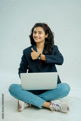 indian girl seated on a white background balances a laptop on her lap