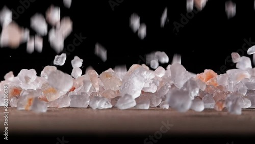 HIMALAYAN SALT crystals fall in slow motion onto a wooden surface. The pink grains scatter beautifully across the dark background.