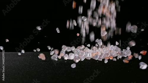Pink Himalayan SALT grains fall in slow motion onto a black background. Macro close-up of translucent crystals used in gourmet cooking and health products.
