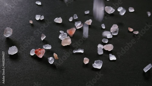 Pink Himalayan SALT crystals fall and bounce across a black surface in slow motion. Close-up shot shows clarity, texture and natural variation of grains.