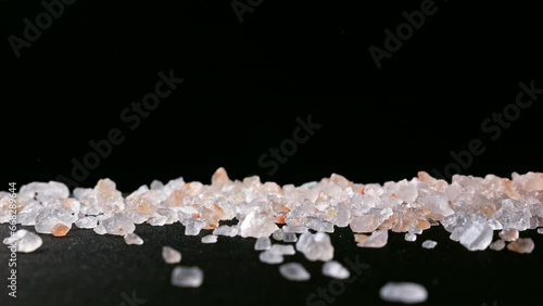 Pink Himalayan SALT crystals falling and scattering on a black surface in slow motion. Macro shot highlighting texture, color and clarity of mineral grains.