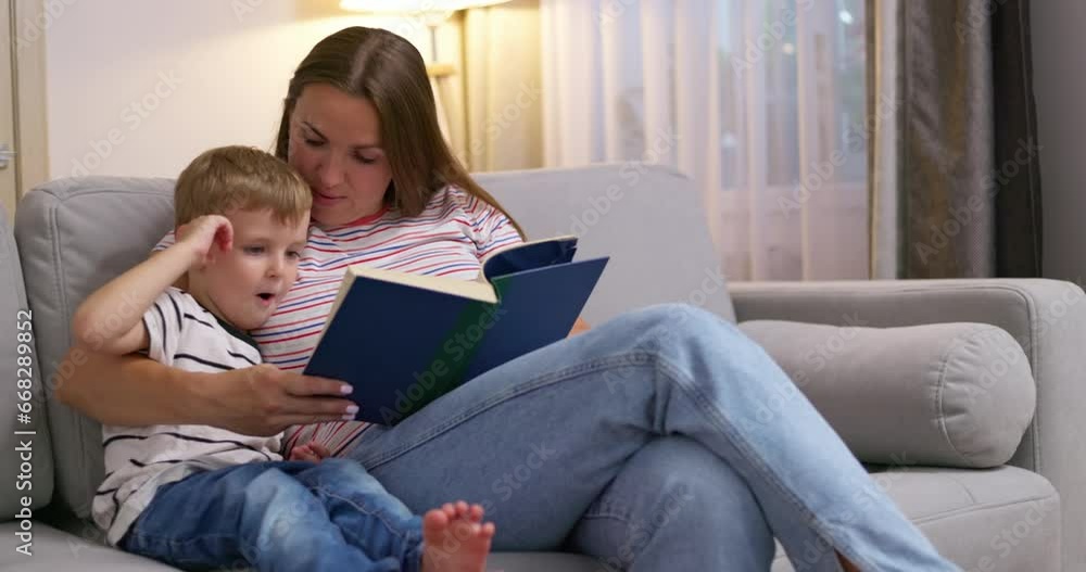 Mother and son are reading a book sitting on a cozy sofa in the living room Mother and son are reading a book sitting on a cozy sofa in the living room