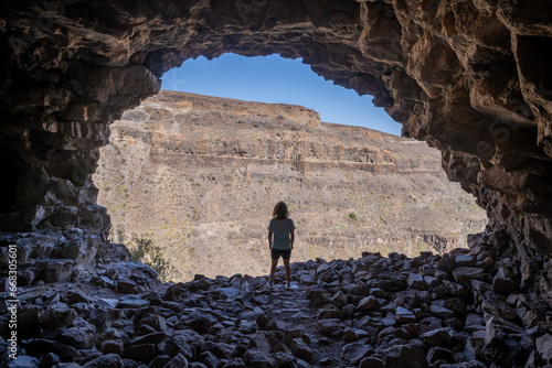 Rear view of a woman standing in the access of a large cave looking outside in the archaeological complex 
