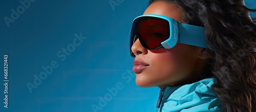 Latin female skier with snowboard goggles alone on blue backdrop