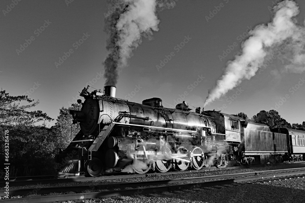 A black and white of an antique coal locomotive spewing both steam and black smoke