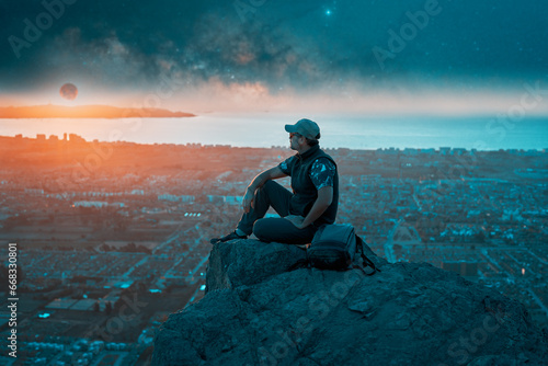 silhouette latin mature man sitting on top of the hill contemplating the moon on the horizon over the city © oscargutzo