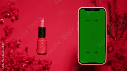 Phone with green screen chroma key on red and pink background close up , top view. Smartphone on summer bright texture studio shot. Composition of rose flowers and make up.  photo