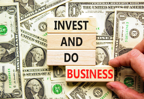 Invest and do business symbol. Concept word Invest and do business on beautiful wooden block. Dollar bills. Beautiful background from dollar bills. Invest and do business concept. Copy space.