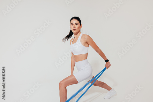 Young female athlete in white sports clothes using a resistance band to train arm