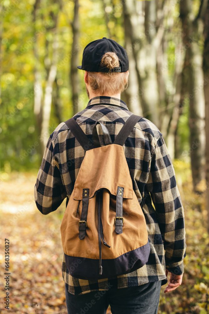 Traveler with a backpack is walking on an road along autumn forest, concept of freedom, travel, hiking and autumn mood, copy space.