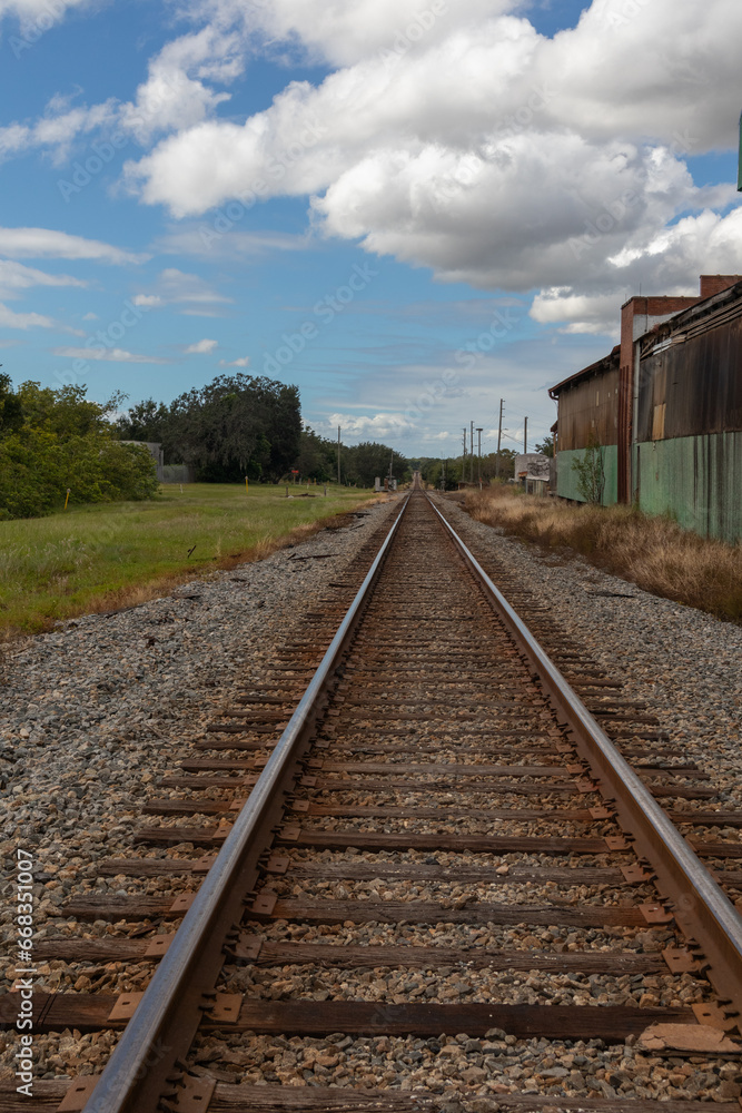 Fototapeta premium Railroad track leading to horizon next to abandoned warehouse