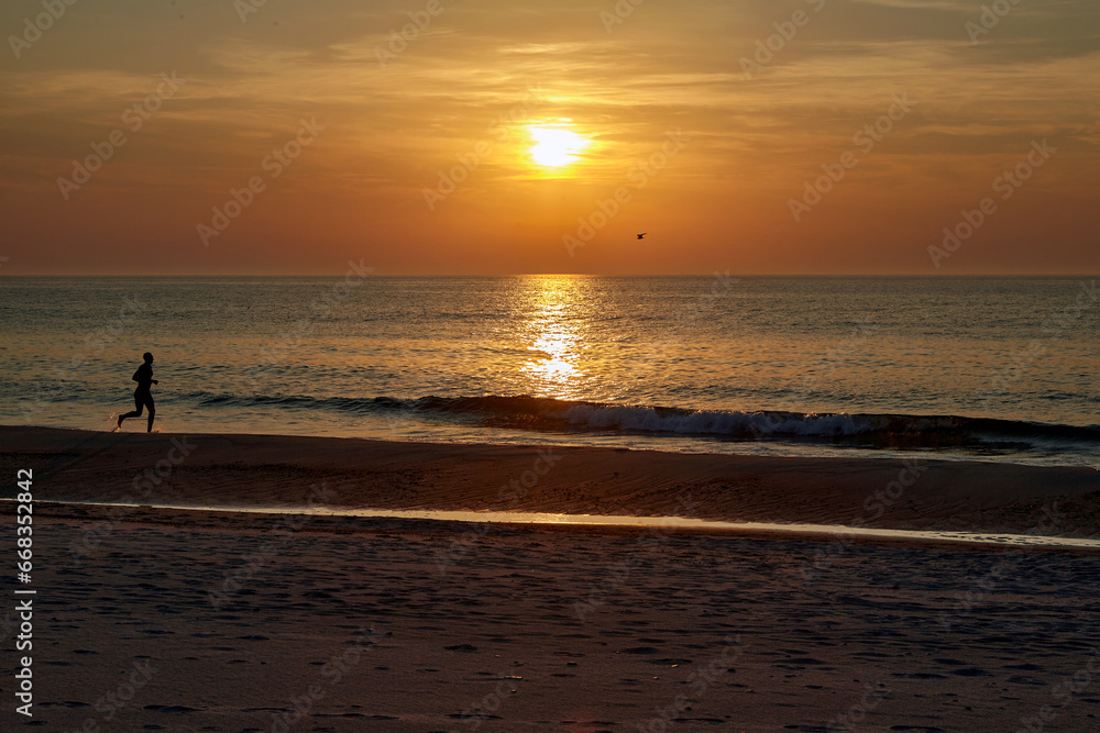 Silhouette of a man running along the seashore against the backdrop of a beautiful golden sunset