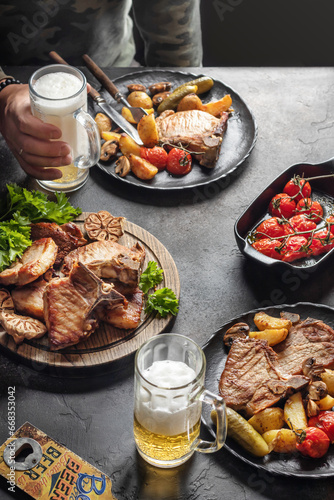 Grilled roasted bbq pork stake served with vegetables and beer on brown table background. Party table