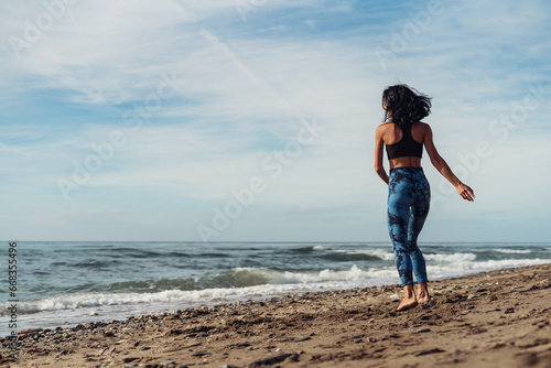 A beautiful brunette girl is dancing on the beach by the sea on the sand
