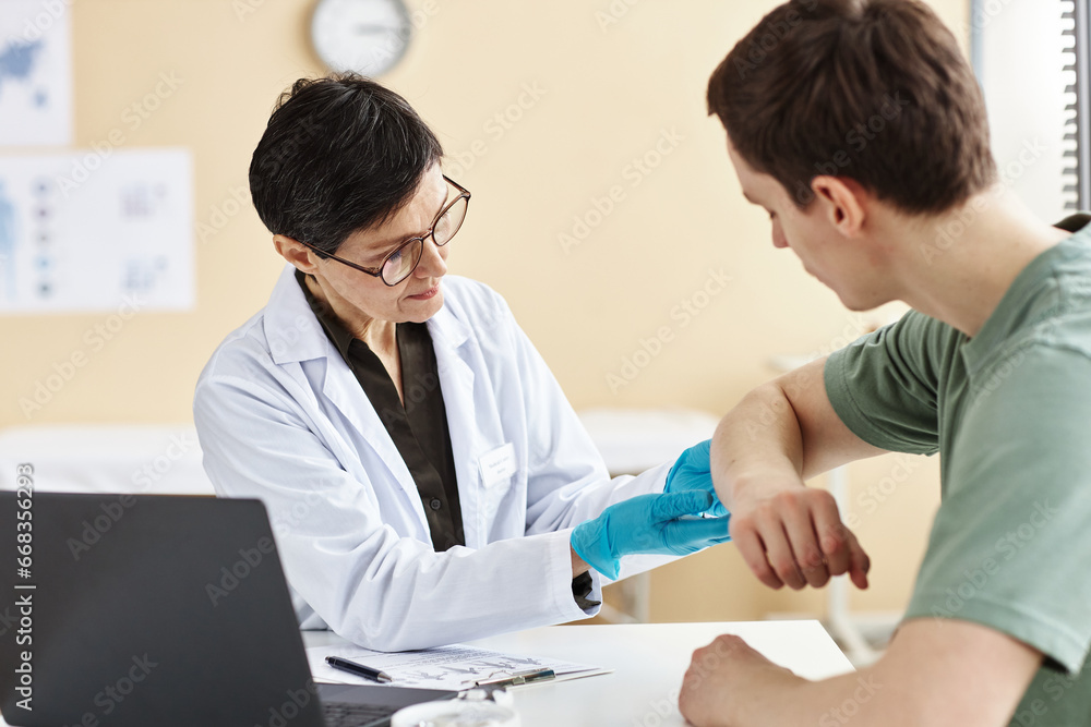 Portrait of mature female doctor inspecting patient with skin rash during consultation in dermatology clinic Portrait of mature female doctor inspecting patient with skin rash during consultation in dermatology clinic