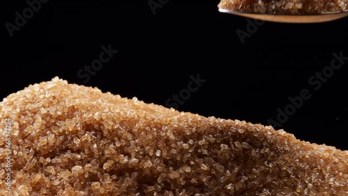 Brown cane SUGAR being scooped with a spoon against a black background. Macro shot showing crystal texture and golden color.